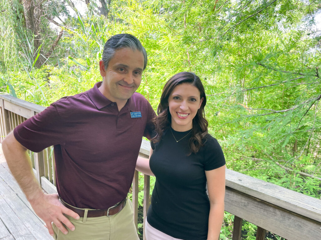 a man and woman standing on a deck in front of trees